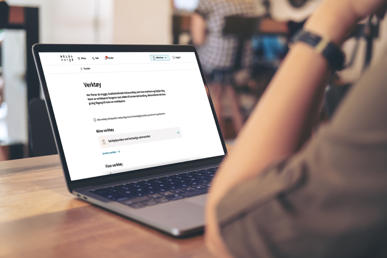 Illustrasjonsbilde av person som sitter på kafe, forran en bærbar pc. På skjermen er Vekrtøy-siden på Helsenorge fremme.